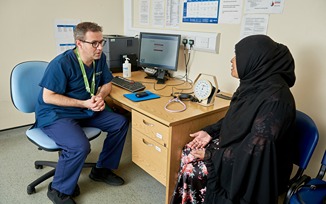 A person sitting in a General Practitioner (GP) surgery room discussing their health with the GP